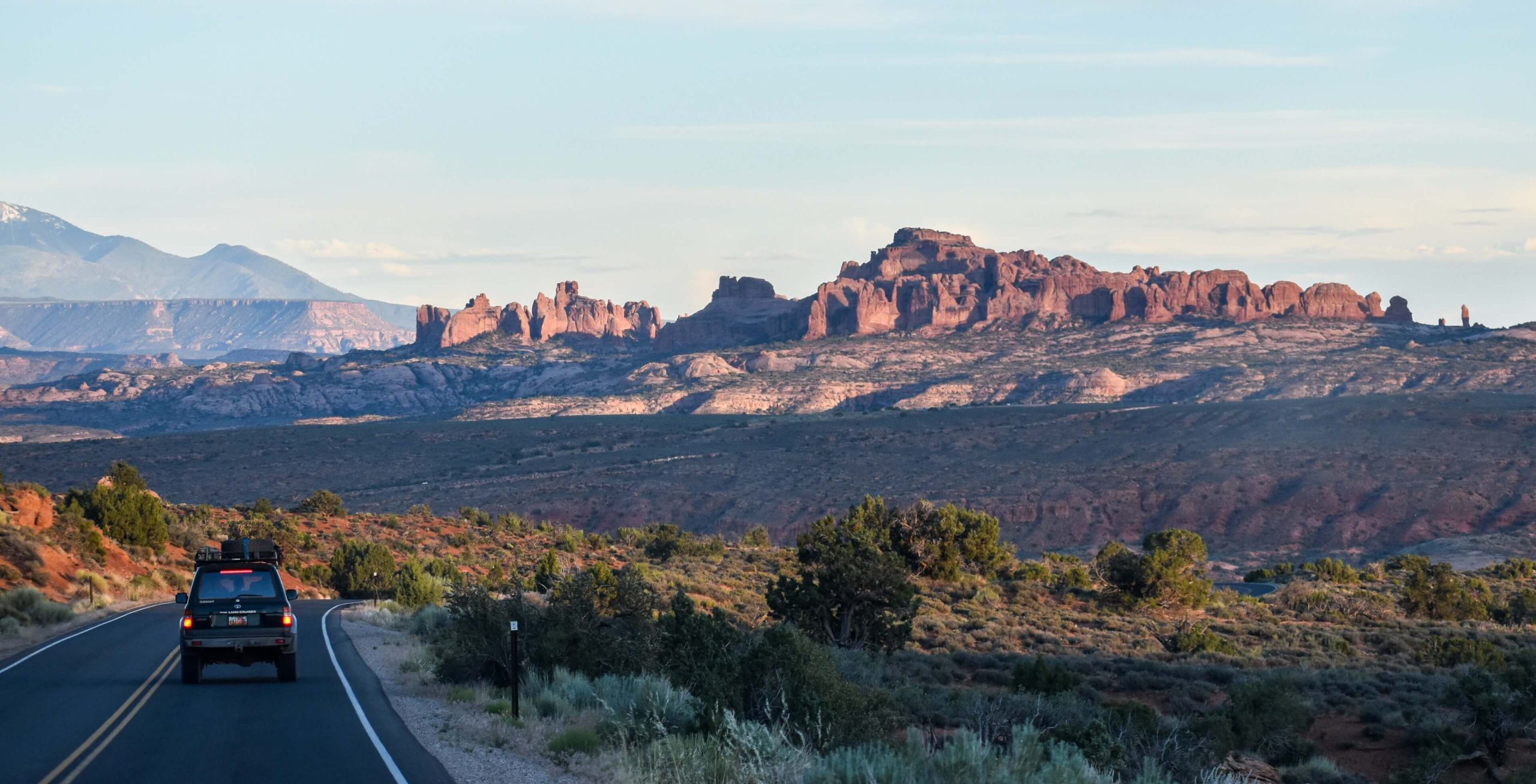 An SUV drives on a winding road near Lionsback Resort surrounded by Moab's beautiful desert scenery.