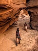 Two people hiking through red rocks and slot canyons in Moab near Lionsback Resort.