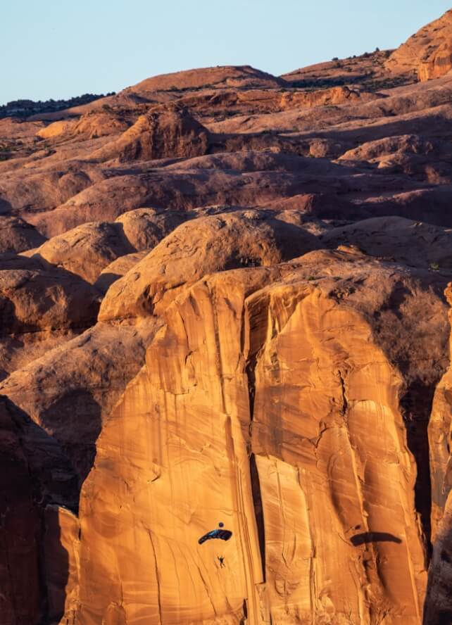 A person parachuting in front of a rock face on a sky diving experience near Lionsback Resort.