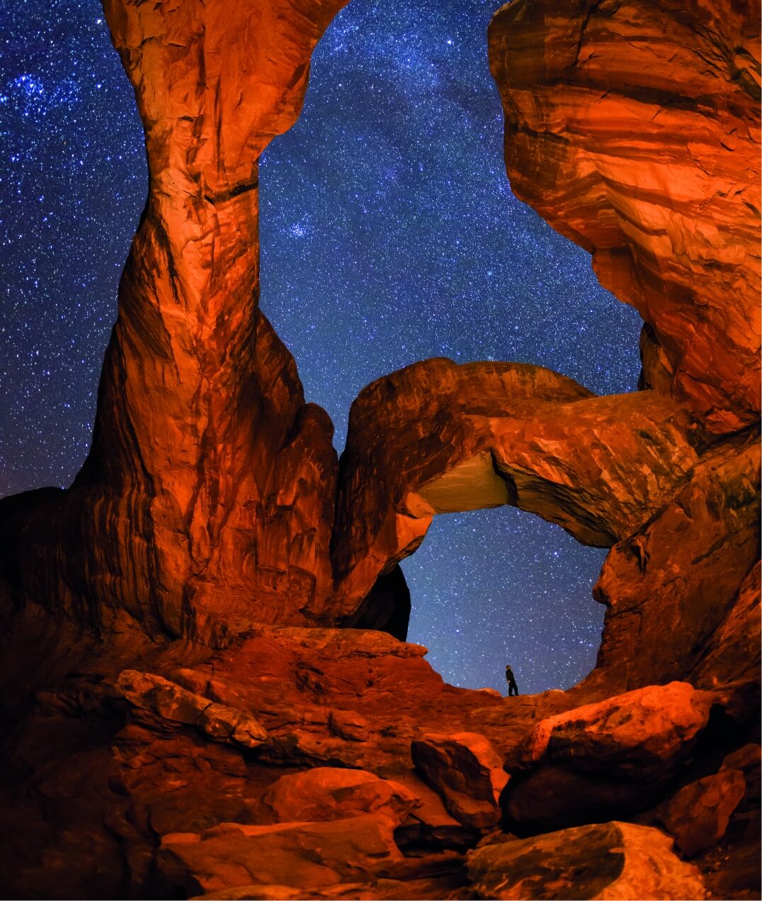 A hiker taking in the stunning starry sky under rocky arches near Lionsback Resort in Moab Utah.
