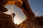 A man climbing the rocks underneath an arch at Arches National Park in Moab near Lionsback Resort.