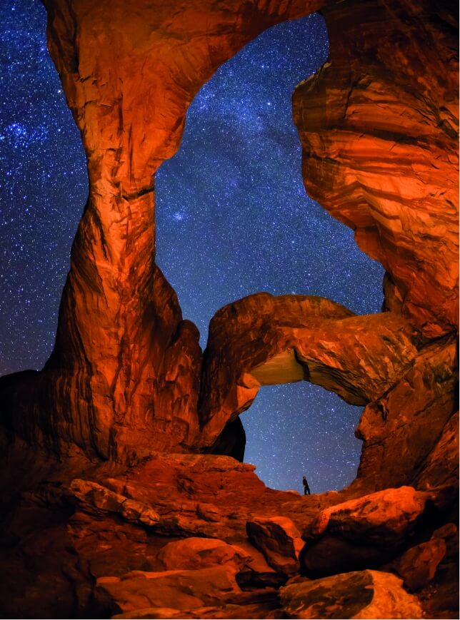 A hiker taking in the stunning starry sky under rocky arches near Lionsback Resort in Moab Utah.