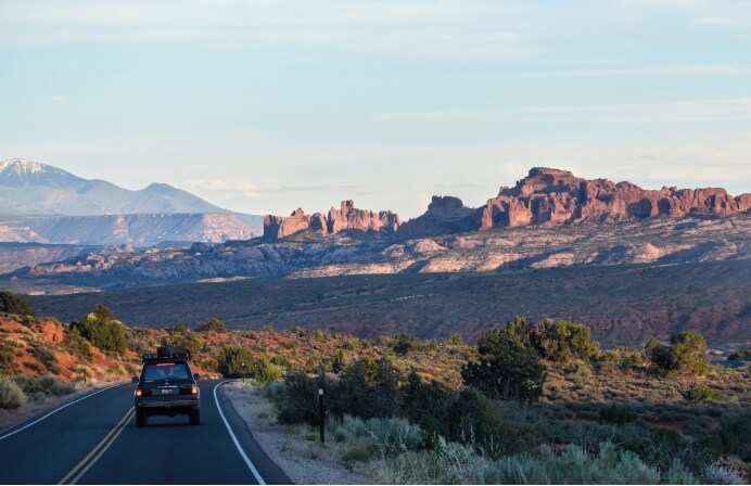 An SUV drives on a winding road near Lionsback Resort surrounded by Moab's beautiful desert scenery.
