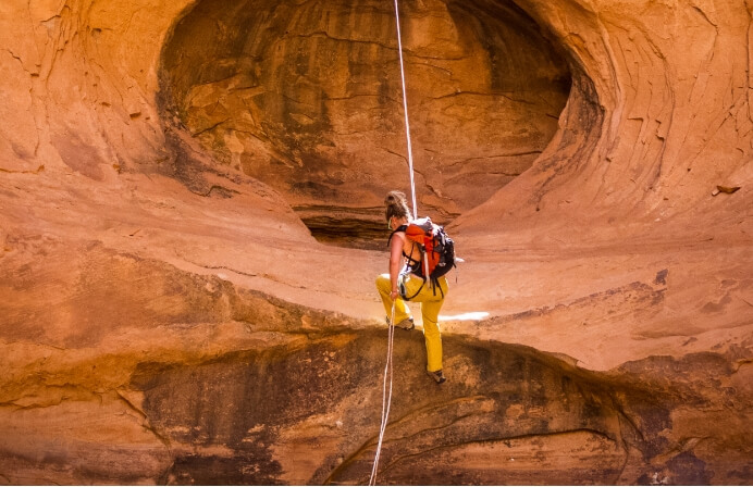 A canyoneer rock climbing in a red rock canyon in Moab near Lionsback Resort.