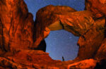 A hiker taking in the stunning starry sky under rocky arches near Lionsback Resort in Moab Utah.
